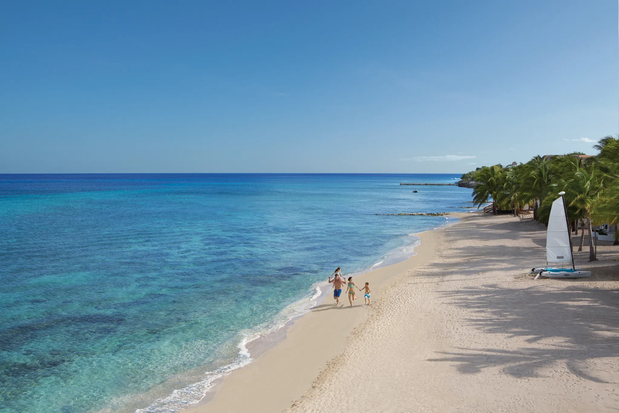 Family playing on the beach at Dreams Cozumel Cape Resort & Spa with ocean hammocks in the background.