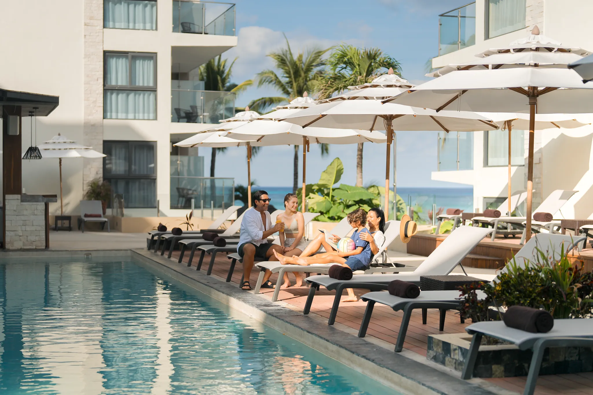 Family relaxing on lounge chairs by the pool at Dreams Cozumel Cape Resort & Spa.