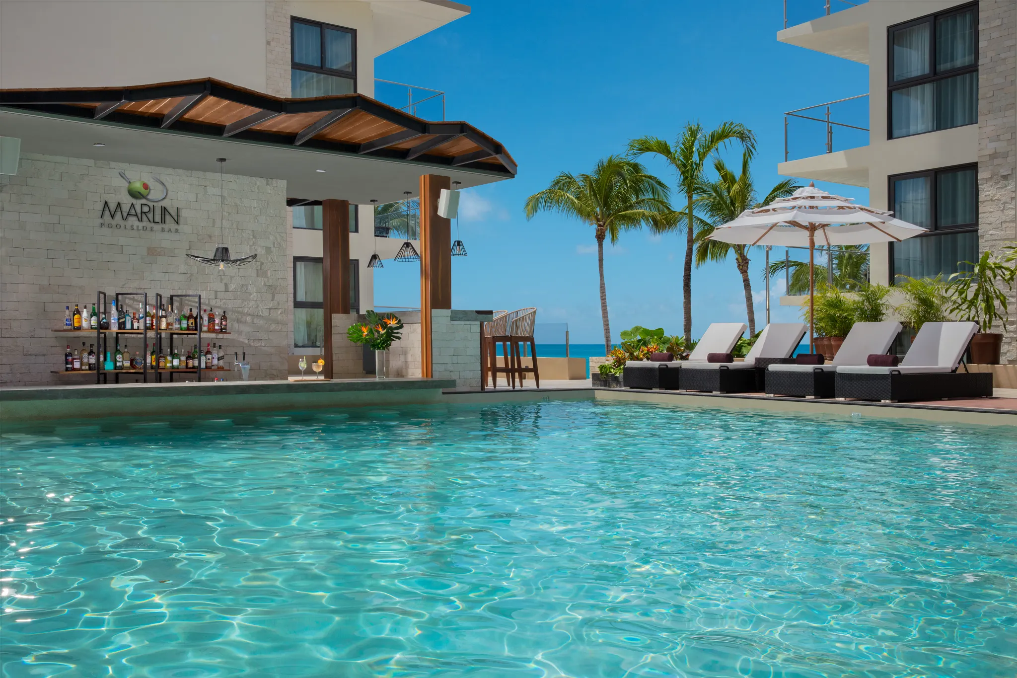 Marlin Pool Bar at Dreams Cozumel Cape Resort & Spa featuring a swim-up bar, turquoise pool, palm trees, and ocean views.